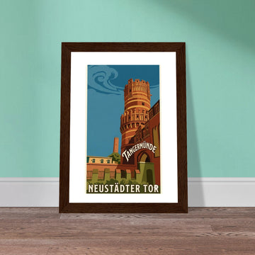 Ein gerahmtes Poster im Retro-Stil an einer mintgrünen Wand. Es zeigt das Neustädter Tor in Tangermünde in warmen Orange-, Rot- und Blautönen, inspiriert von Vintage-Reiseplakaten. Der Schriftzug ‚Tangermünde‘ ist schwungvoll über dem Torbogen platziert, unten steht ‚Neustädter Tor‘ in einer klassischen serifenlosen Schrift.