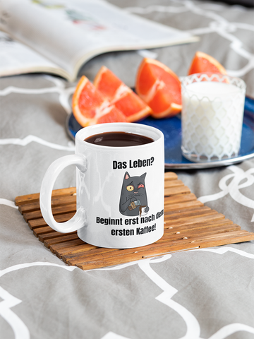 Illustration einer schwarzen Katze, die sehr muffelig und müde ausschaut. Daher auch der Text: Das leben? Beginnt erst nach Kaffee!