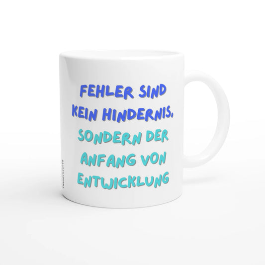 Weiße Keramiktasse mit dem blauen Schriftzug „Fehler sind kein Hindernis, sondern der Anfang von Entwicklung“ auf weißem Hintergrund.