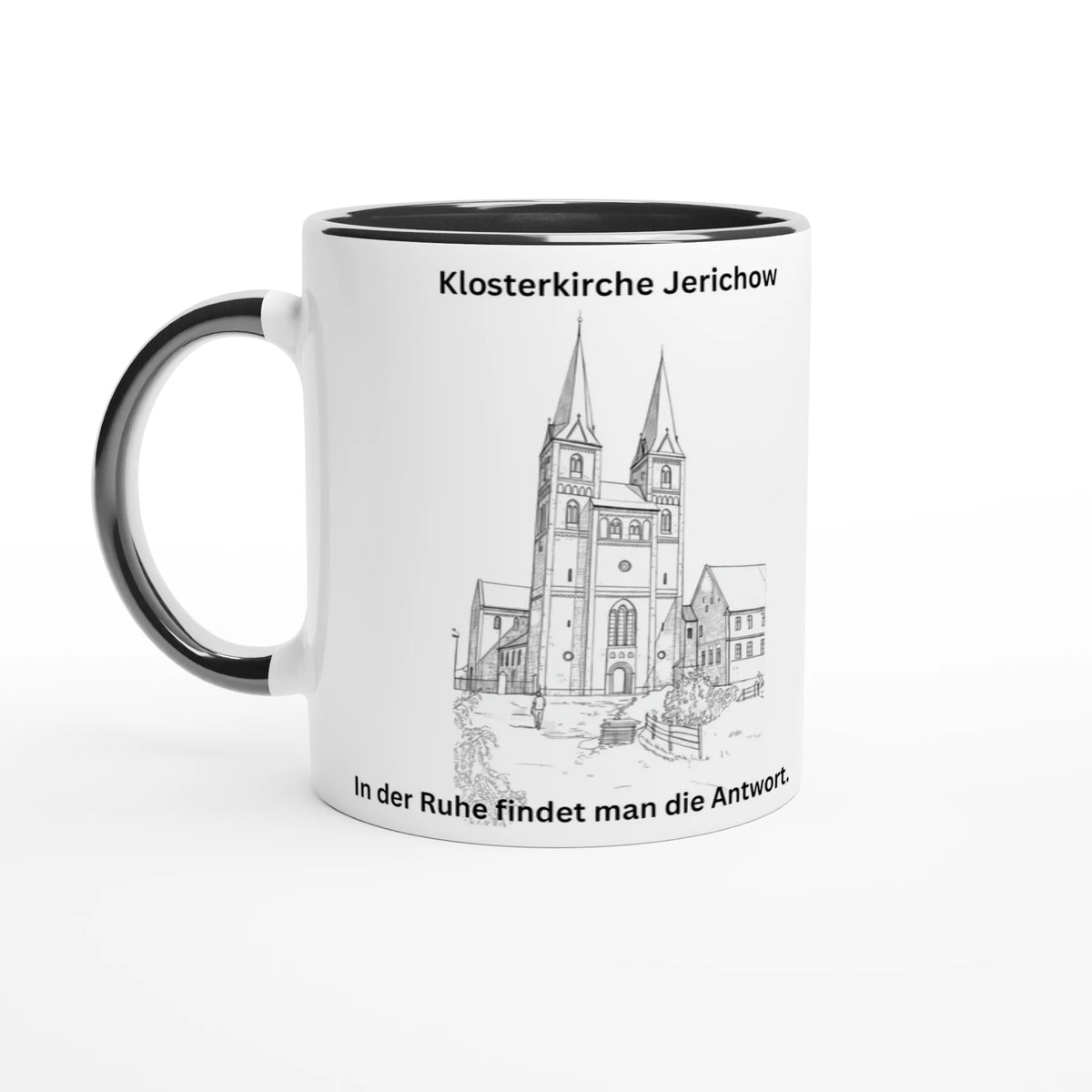 Weiße Kaffeetasse mit schwarzem Henkel und schwarzer Innenseite. Auf der Vorderseite ist eine detailreiche Bleistiftzeichnung der Klosterkirche Jerichow abgebildet. Über der Illustration steht der Schriftzug „Klosterkirche Jerichow“, am unteren Rand steht der inspirierende Spruch: „In der Ruhe findet man die Antwort.“