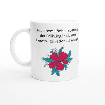 Weiße Keramiktasse mit Blumenmotiv und dem Spruch „Mit einem Lächeln beginnt der Frühling in deinem Herzen – zu jeder Jahreszeit“.