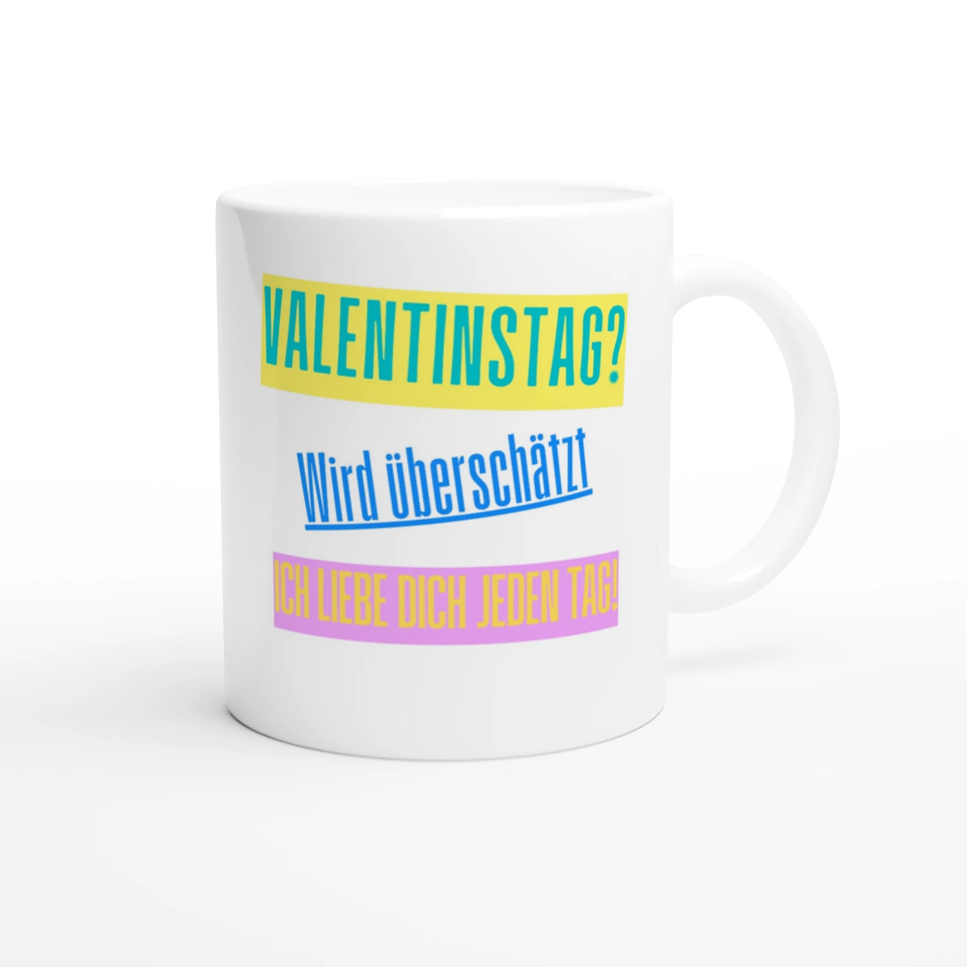 Weiße Keramiktasse vor weißem Hintergrund. Der Aufdruck zeigt drei Textblöcke: Oben „VALENTINSTAG?“ in Blau auf gelbem Balken, mittig „Wird überschätzt“ in Blau, unten „ICH LIEBE DICH JEDEN TAG!“ in Gelb auf rosa Balken.