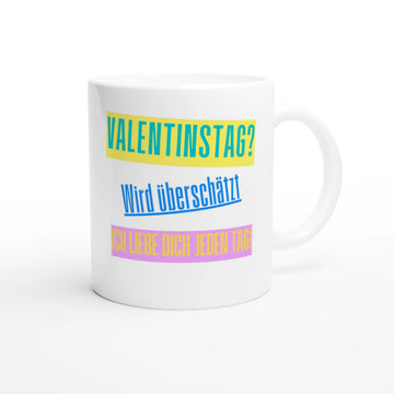 Weiße Keramiktasse vor weißem Hintergrund. Der Aufdruck zeigt drei Textblöcke: Oben „VALENTINSTAG?“ in Blau auf gelbem Balken, mittig „Wird überschätzt“ in Blau, unten „ICH LIEBE DICH JEDEN TAG!“ in Gelb auf rosa Balken.