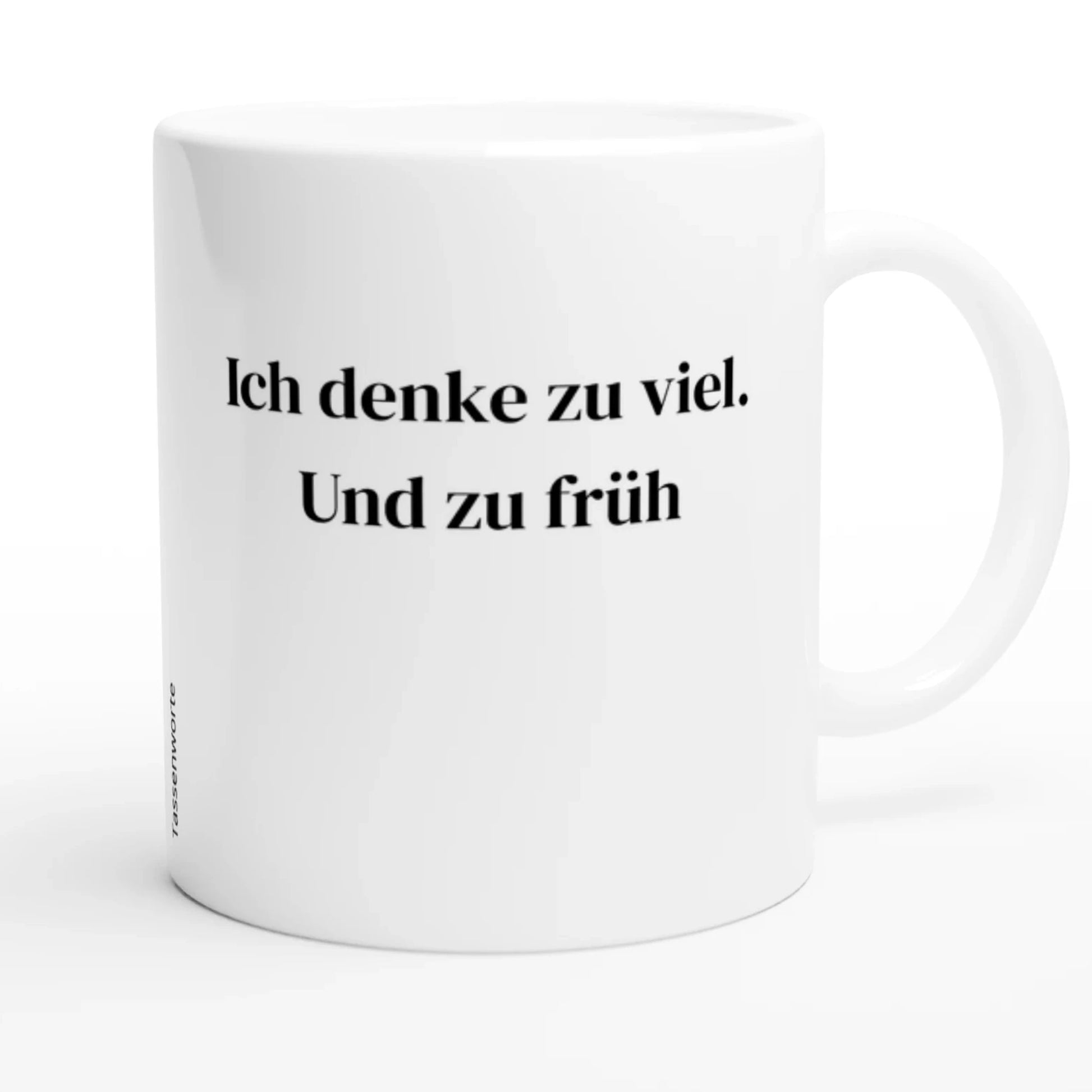 Produktbild einer weißen Tasse der Marke ‚Tassenworte‘. Auf der Vorderseite steht zentriert in eleganter, schwarzer Serifenschrift der Spruch: ‚Ich denke zu viel. Und zu früh.‘ Die Tasse ist leicht nach rechts gedreht, sodass der Henkel sichtbar ist. Seitlich am Rand ist dezent der Markenname ‚Tassenworte‘ vertikal aufgedruckt. Das Bild ist hell, clean und minimalistisch.